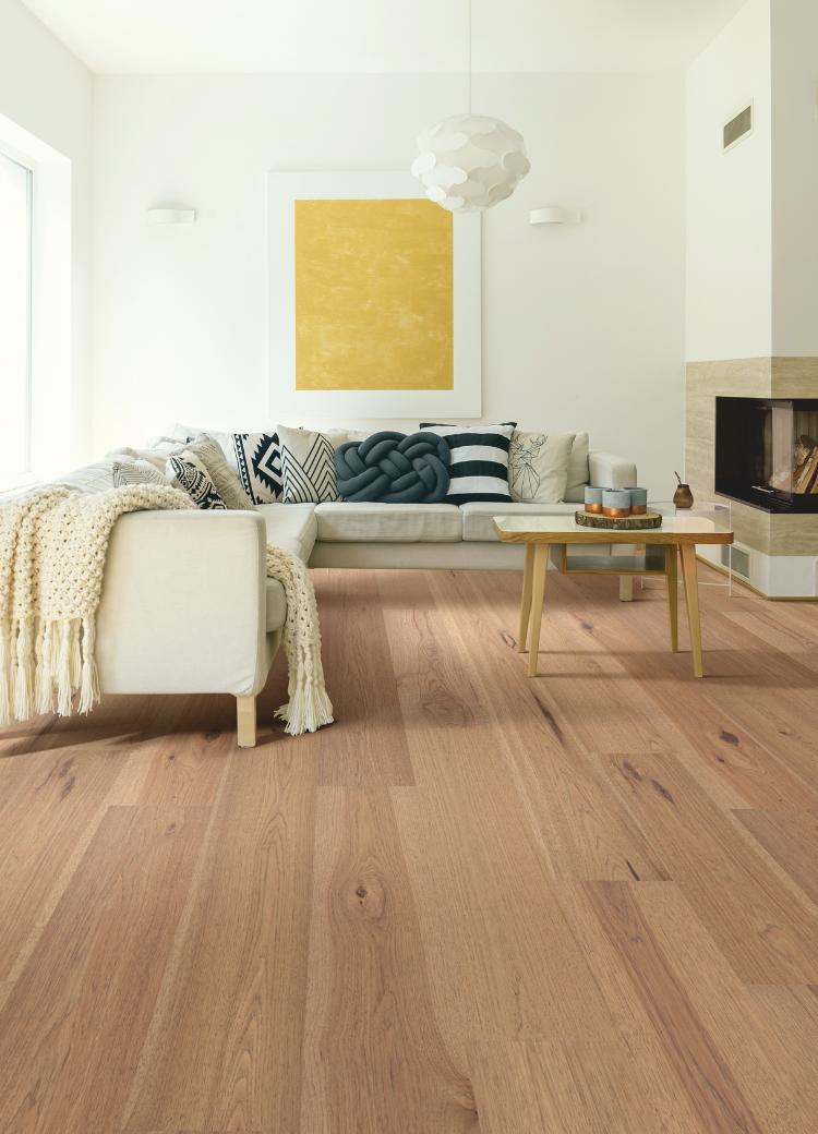 warm toned hardwood flooring in living room with cream couch, fireplace, and lighting.